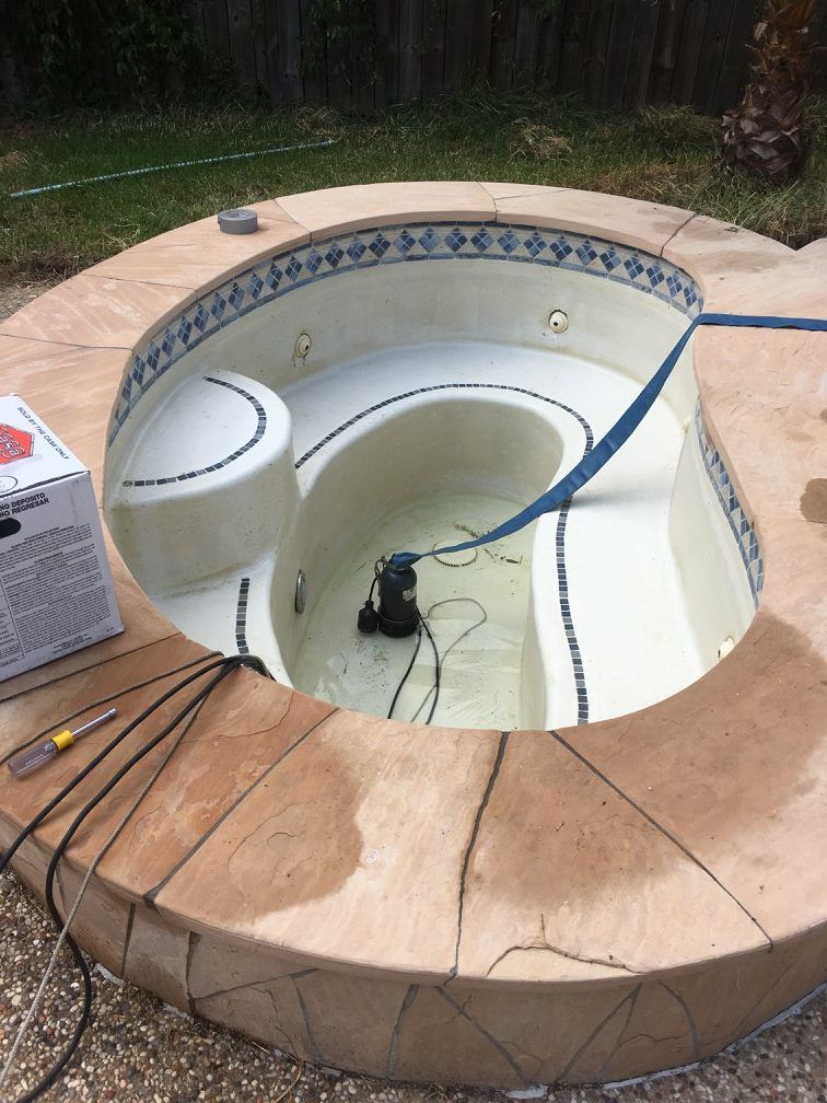 A partially filled, circular spa with a blue hose, and a pump inside. The spa has blue and white tile detail.