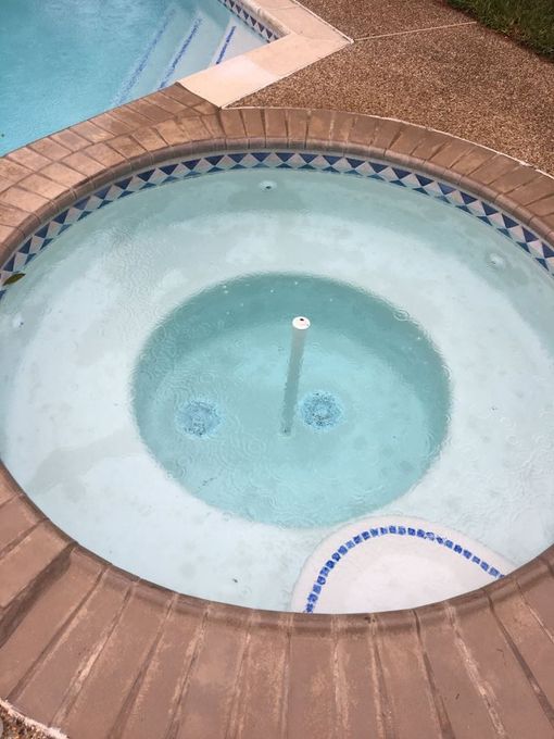 A round, in-ground spa filled with light blue water, next to a larger swimming pool.