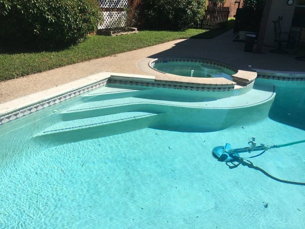 Swimming pool with steps, connected to a hot tub, next to a patio and green grass.