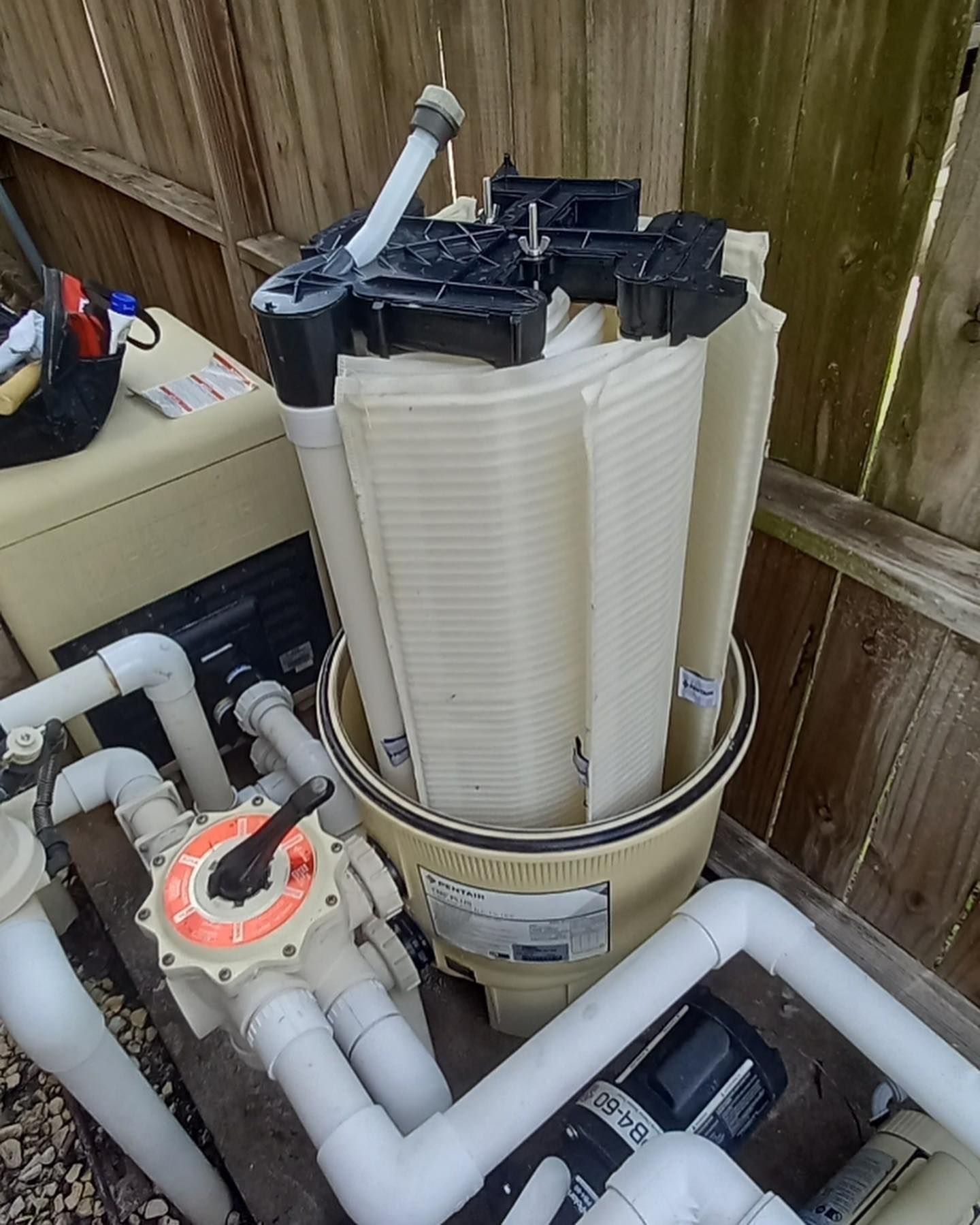 Pool filter with multiple vertical pleated cartridges inside a cylindrical beige housing, surrounded.