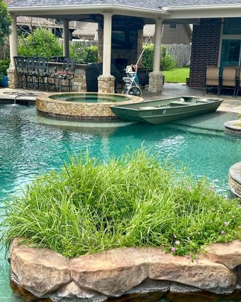 A green rowboat in a turquoise pool. A built-in hot tub, patio with chairs and bar, and a stone island.