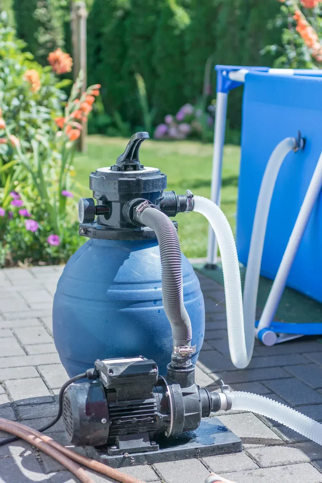 A blue pool filter and pump system on a patio, with hoses connecting to a blue above-ground pool.
