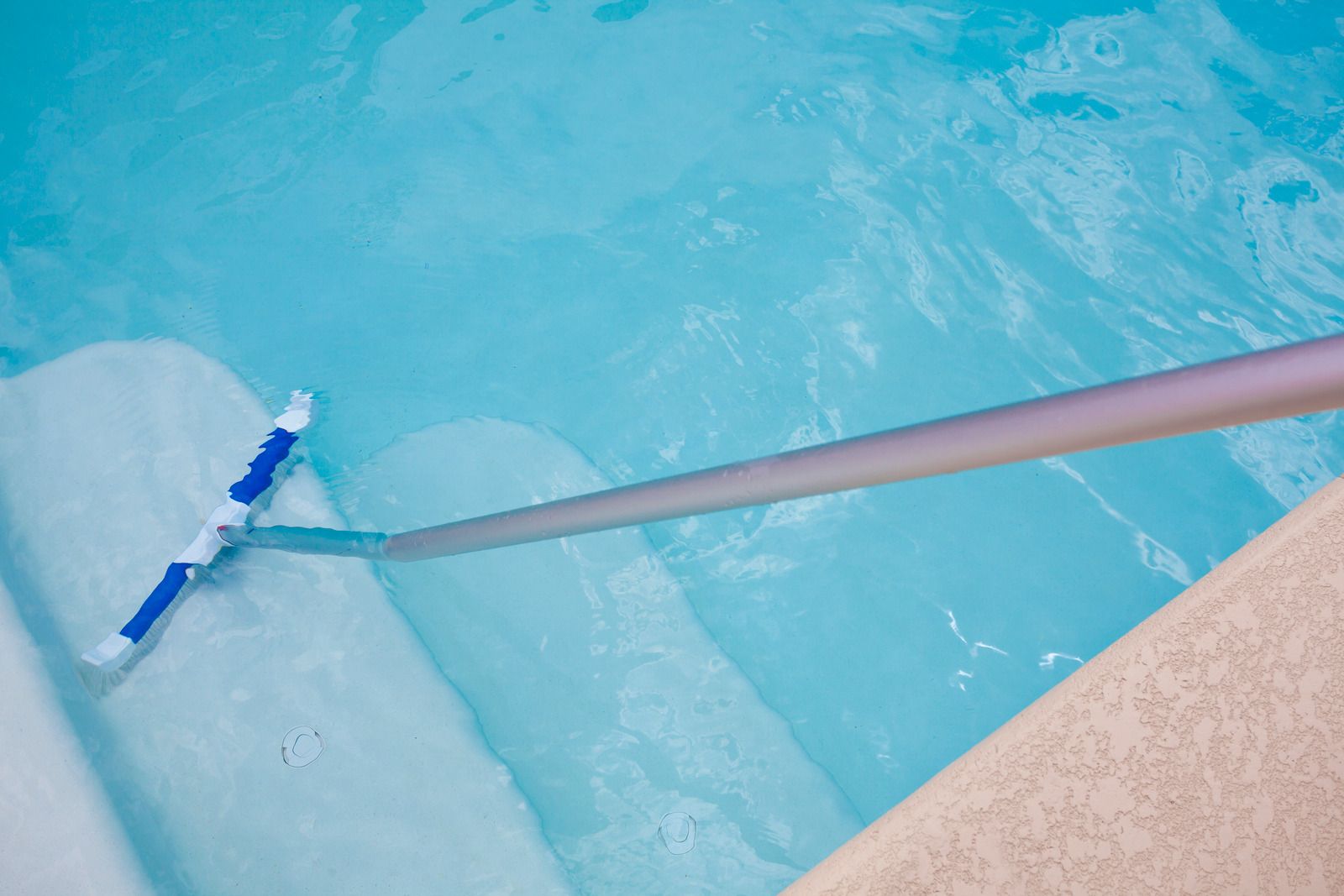 Pool cleaner skimming the clear, blue water of a swimming pool, near the steps.