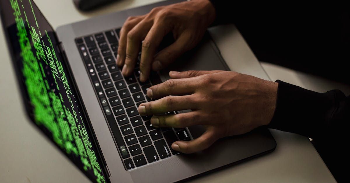 Hands typing on a laptop with green code displayed on the screen.