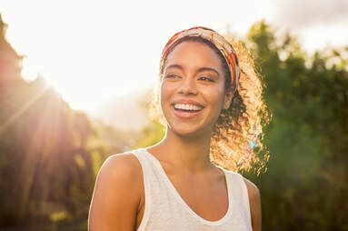 A woman wearing a headband and a white tank top is smiling.