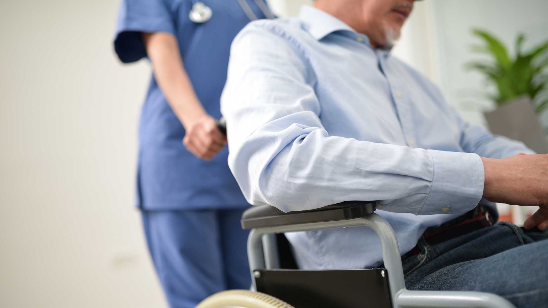 Nurse pushing an elderly man in a wheelchair; indoor, daylight setting.