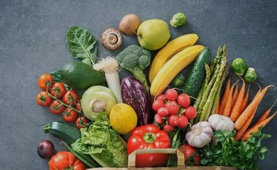 Fresh produce overflowing from a shopping bag: tomatoes, carrots, broccoli, apple, banana, etc.