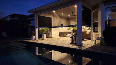 A house with a covered patio and a swimming pool at night.