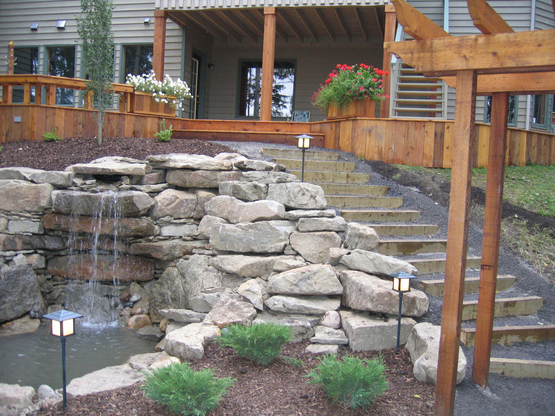 Waterfall in pond surrounded in rocks in backyard garden with wood trellis