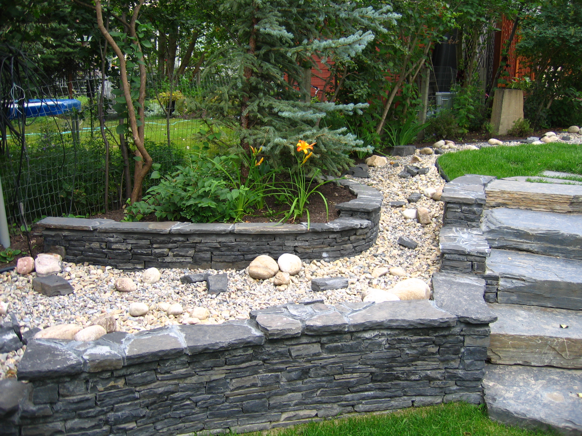 Garden walls and retaining walls together with shrubs and drain rock plus natural stone steps as part of a landscape design by Larix Landscape in Victoria BC