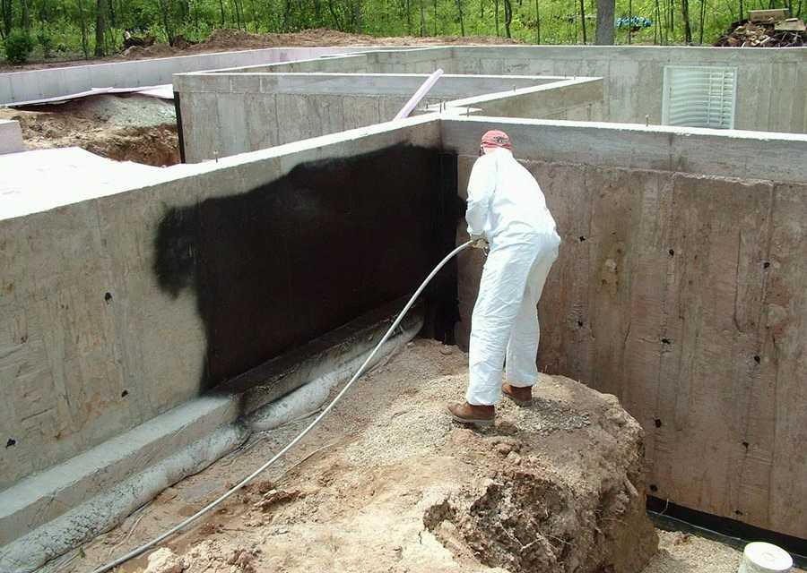 A man spraying a cement foundation with waterproofing spray