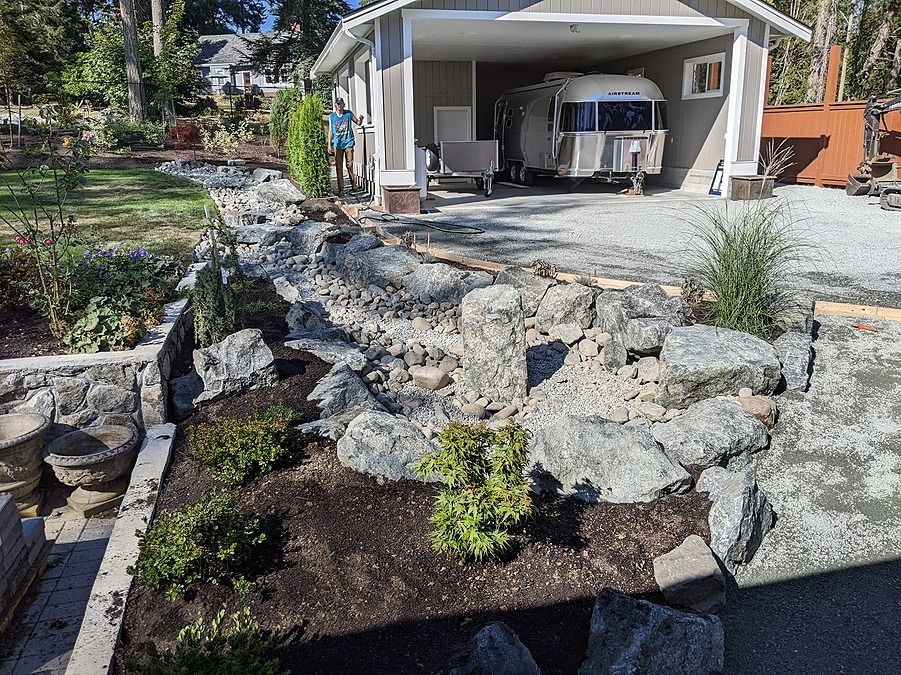 the final result of our custom landscape water feature installation for a Victoria BC client showing rain garden with artificial stream to manage stormwater drainage