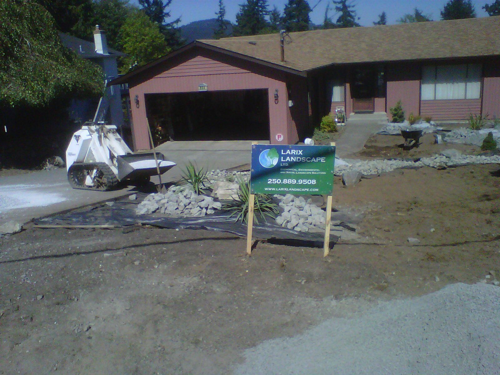 Larix Landscape picket sign planted in excavated property in front of bobcat excavator