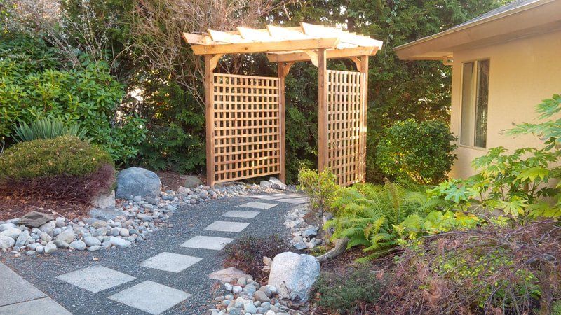 A wooden pergola constructed in back yard with garden designed by Larix Landscape in Victoria BC