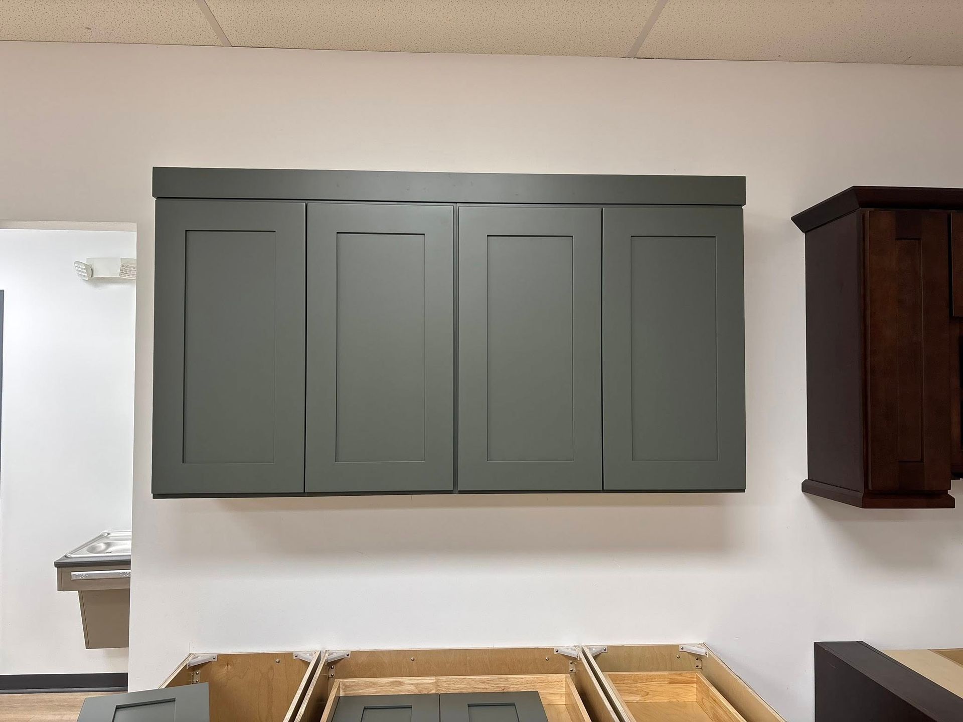 Four gray shaker-style wall cabinets with a matching crown molding mounted on a white wall in a showroom.