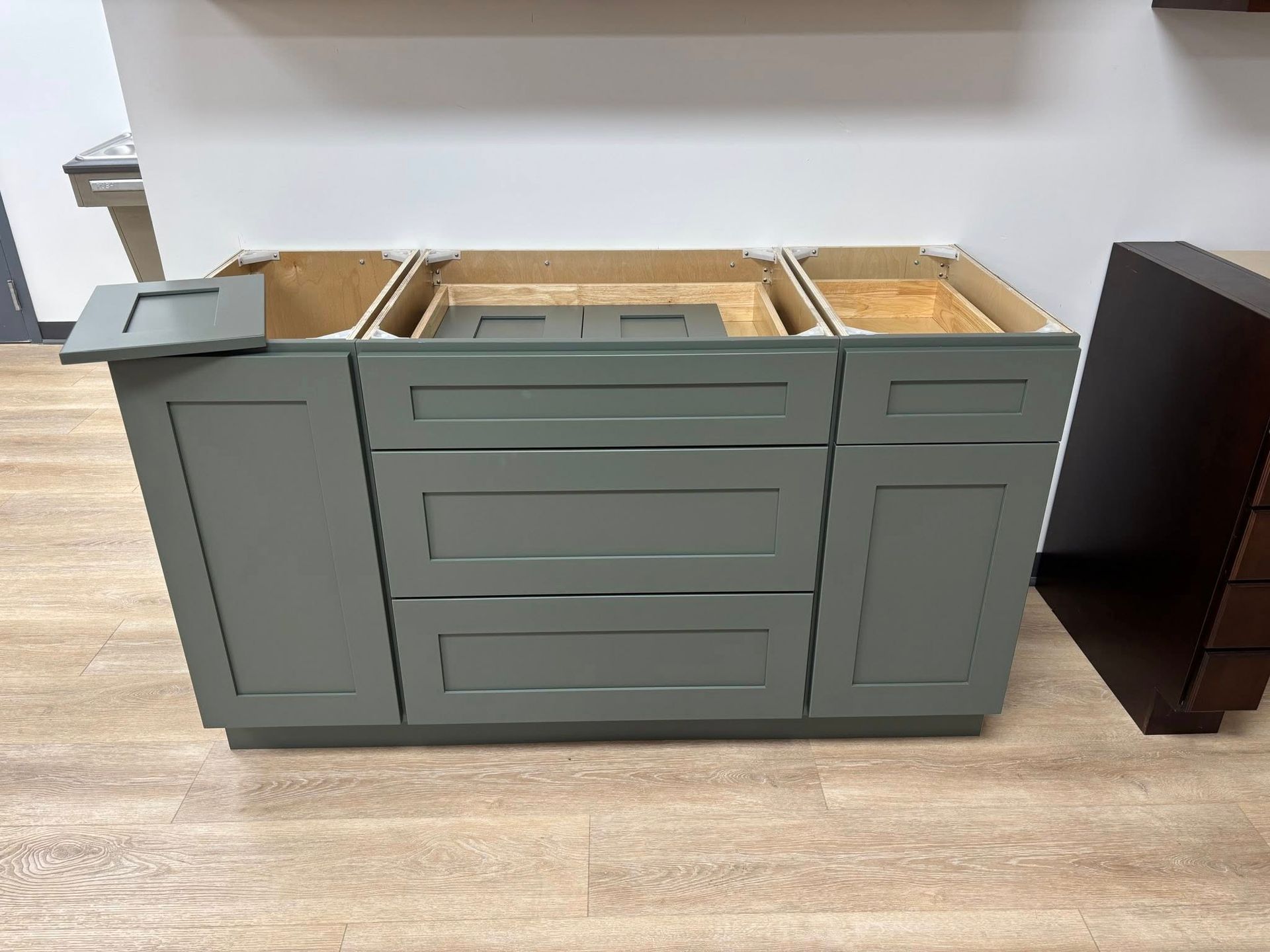 A sage green bathroom vanity base with two side cabinets and two central drawers, displayed in a showroom setting.