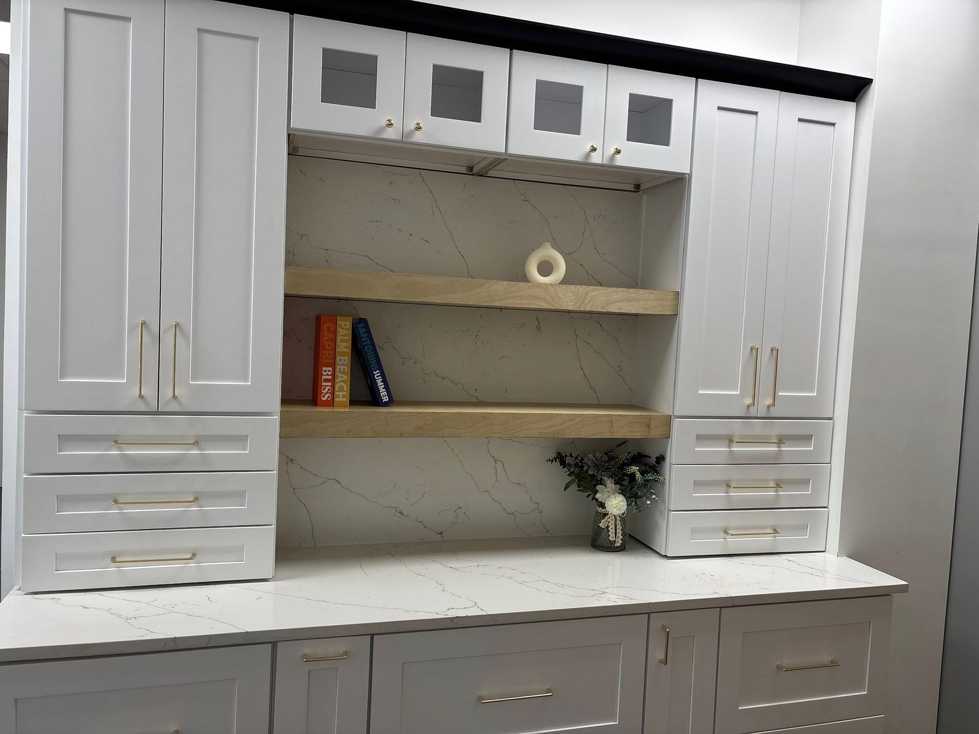White cabinetry with glass-front uppers, open wooden shelves, and marble-style countertops in a bright, modern room.