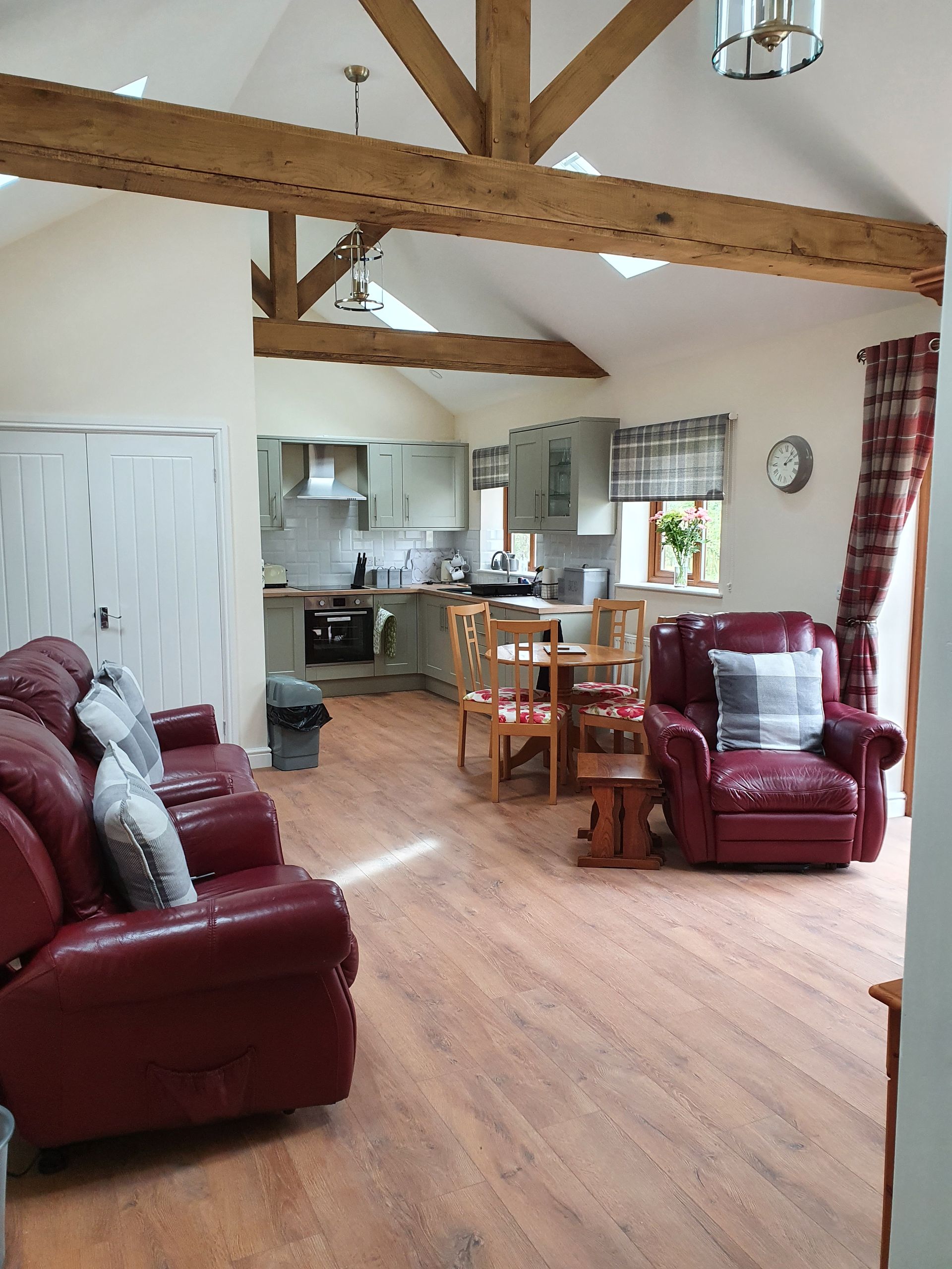 A living room with a red couch and chairs and a kitchen in the background.