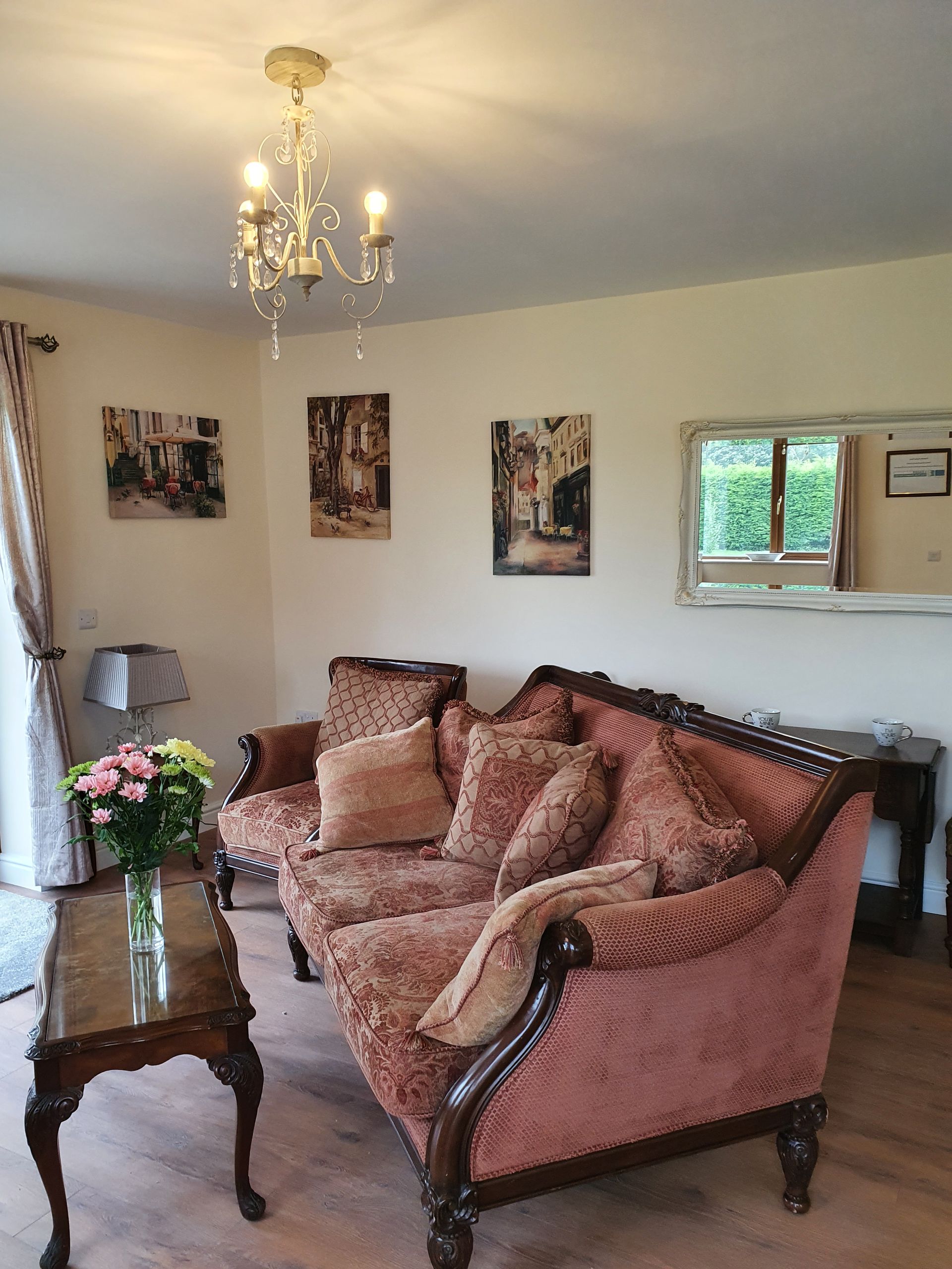 A living room with a couch , table , mirror and chandelier.