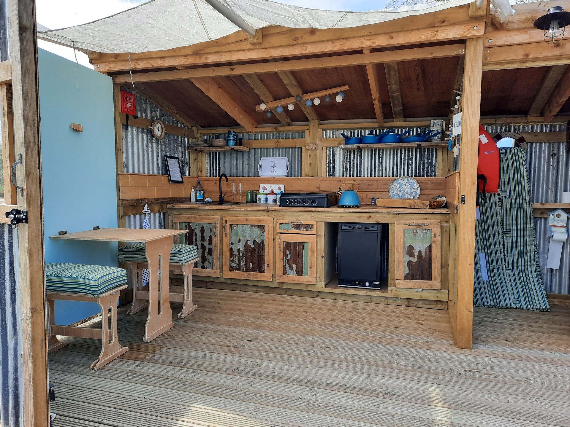 A wooden kitchen with a table and chairs under a roof.