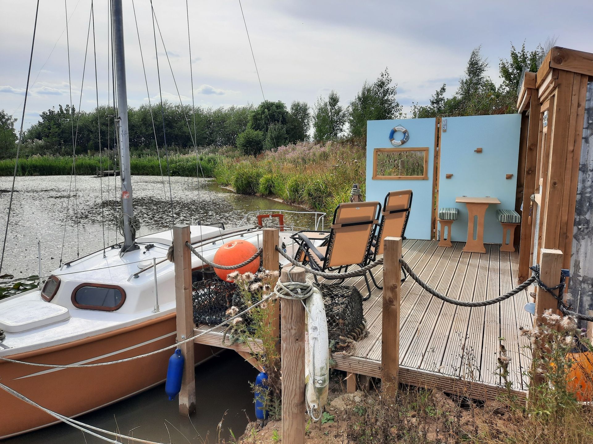 A boat is docked next to a wooden deck with chairs and a table.