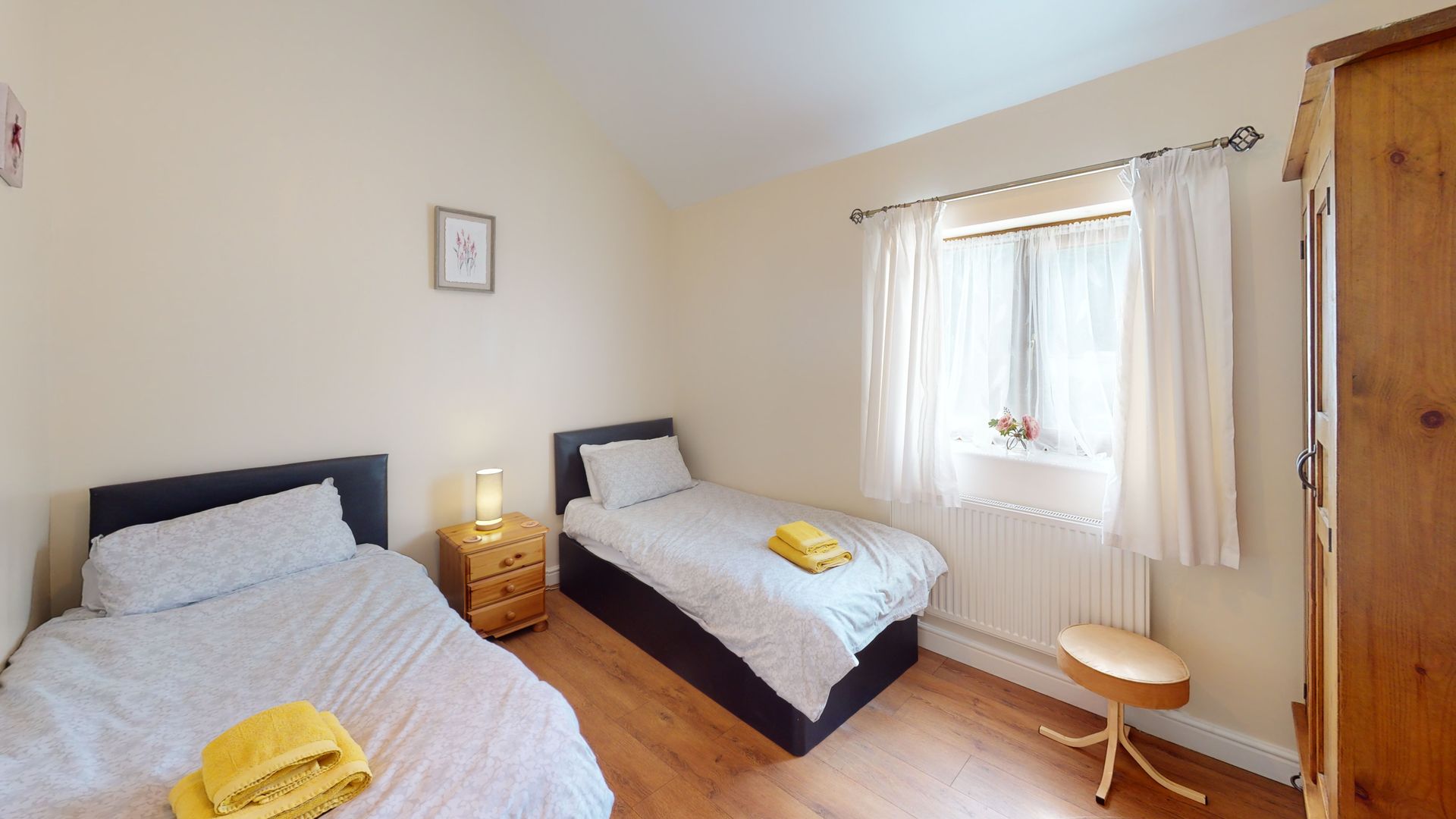 A bedroom with two beds , a nightstand and a window.