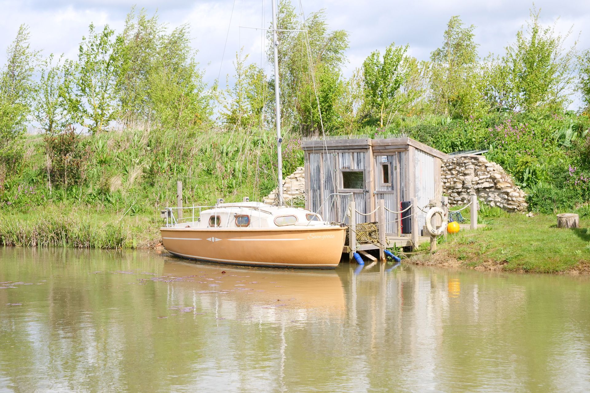 A boat is docked in the water near a wooden shed.
