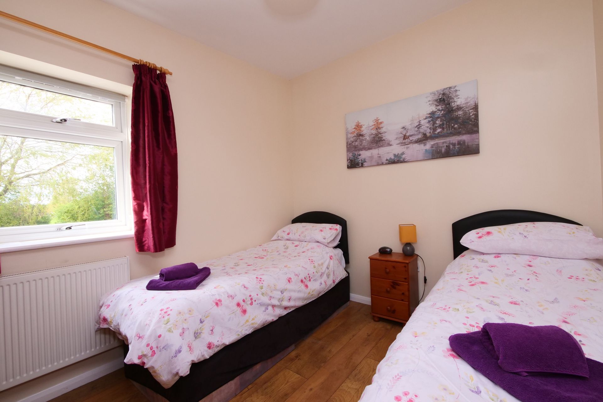 A bedroom with two beds , a nightstand and a painting on the wall.