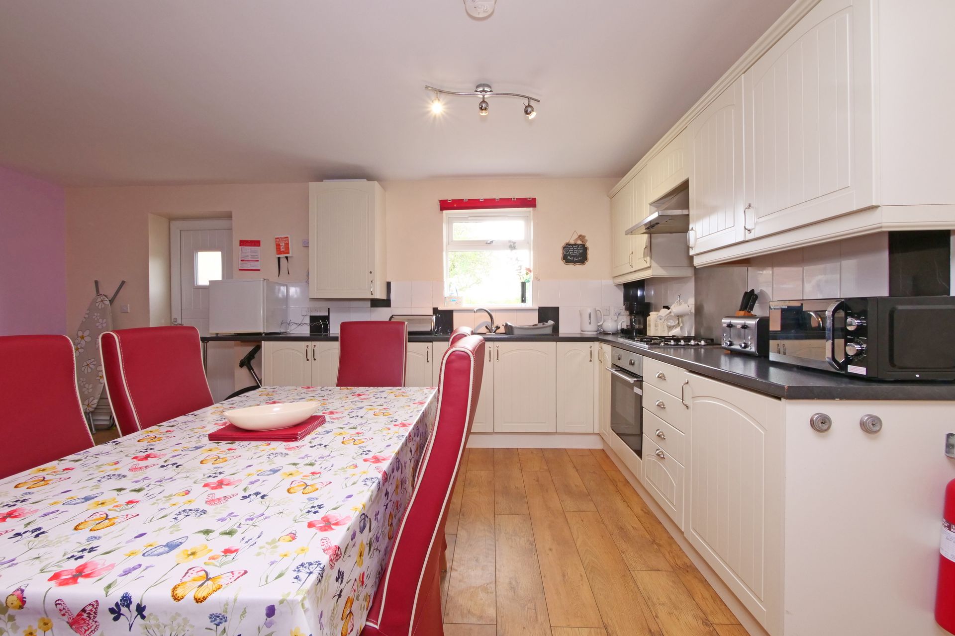 A kitchen with white cabinets and red chairs and a table with a floral tablecloth.