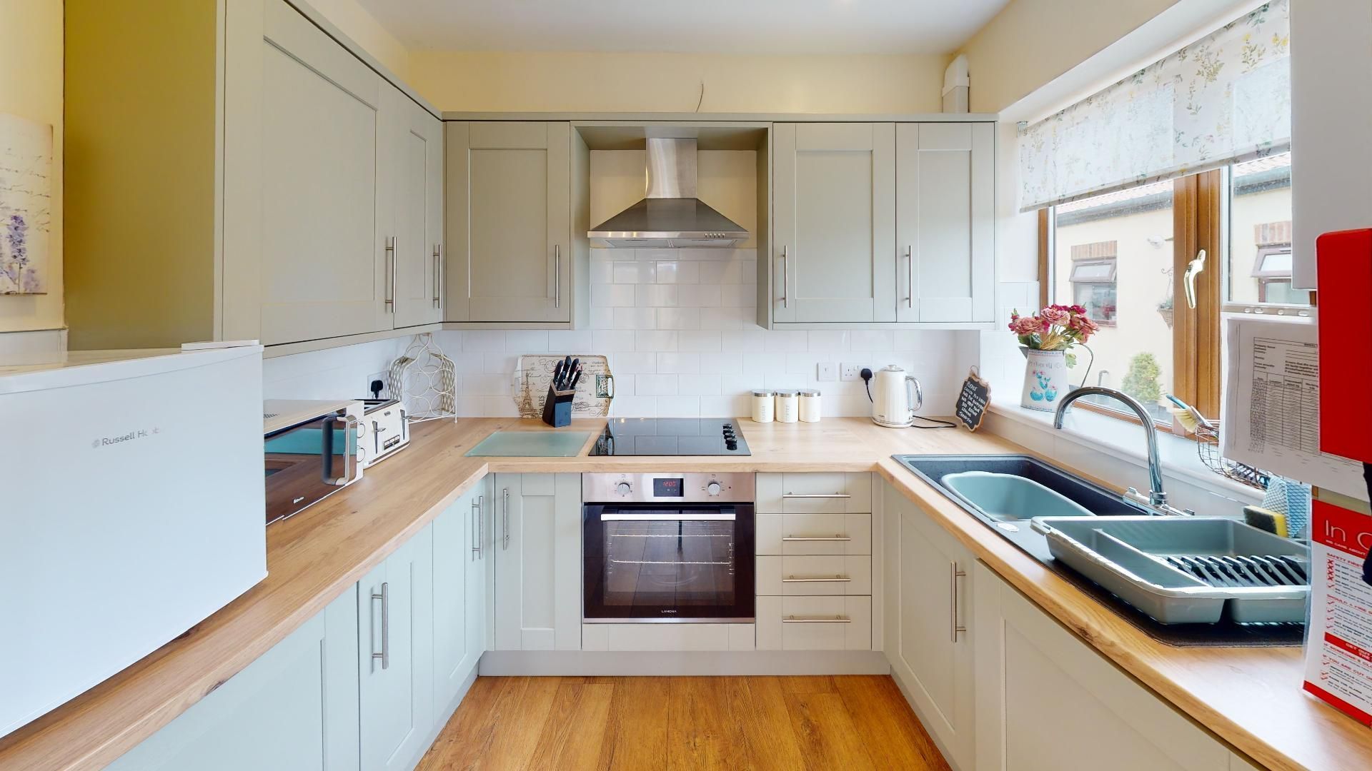A kitchen with white cabinets , an oven, a sink , and a window.