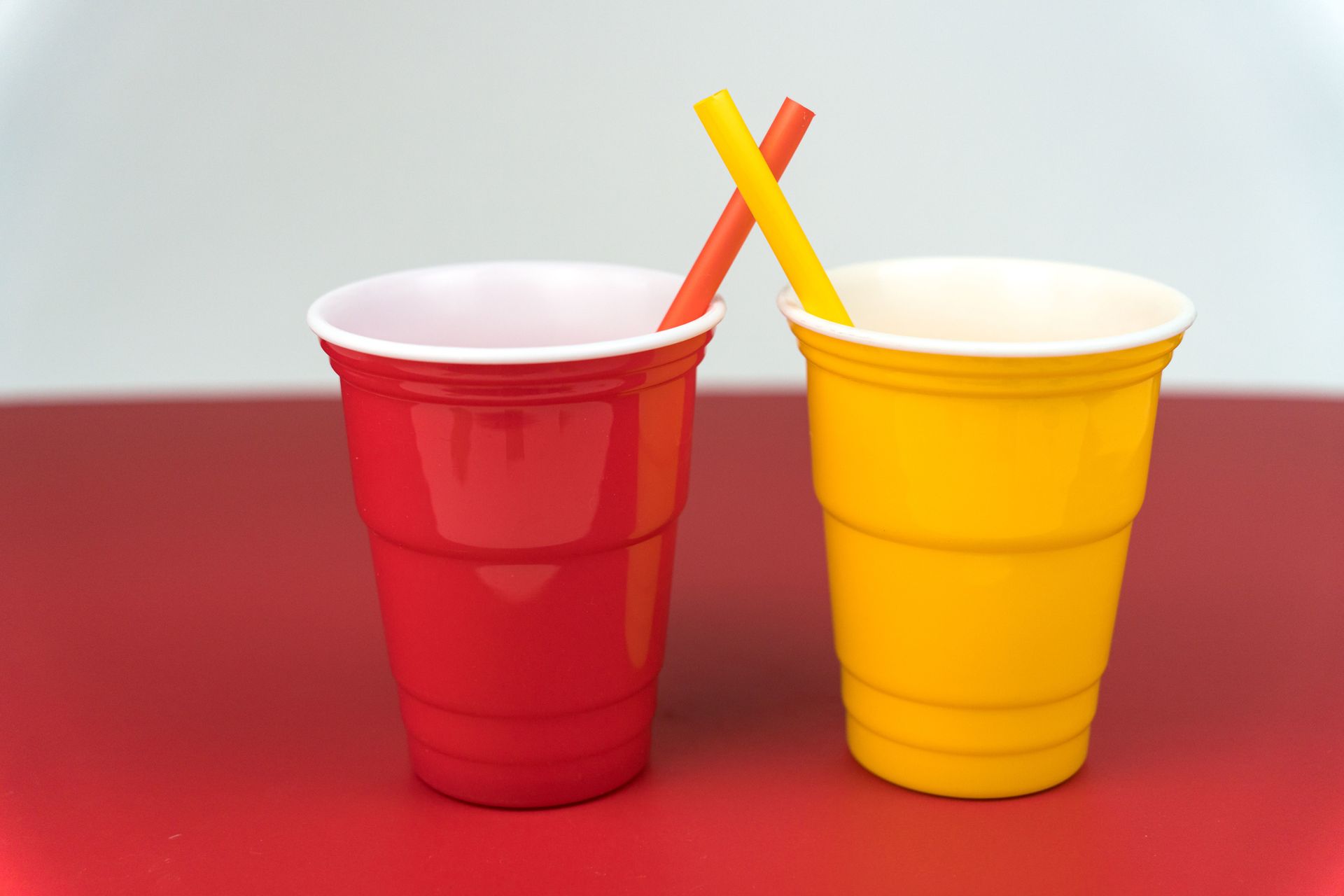 A red cup and a yellow cup with straws in them