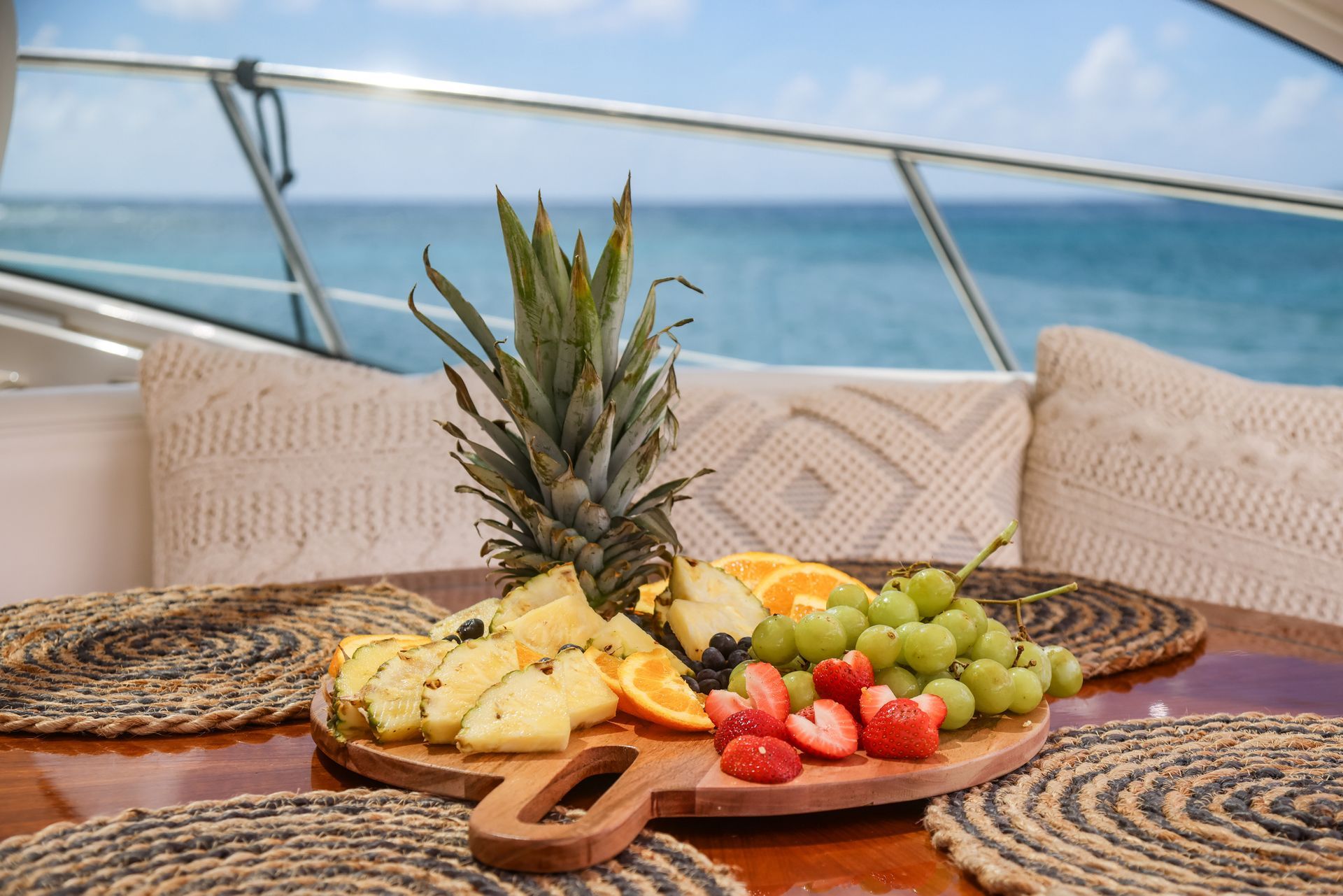 A wooden cutting board filled with fruit and a pineapple on a boat.