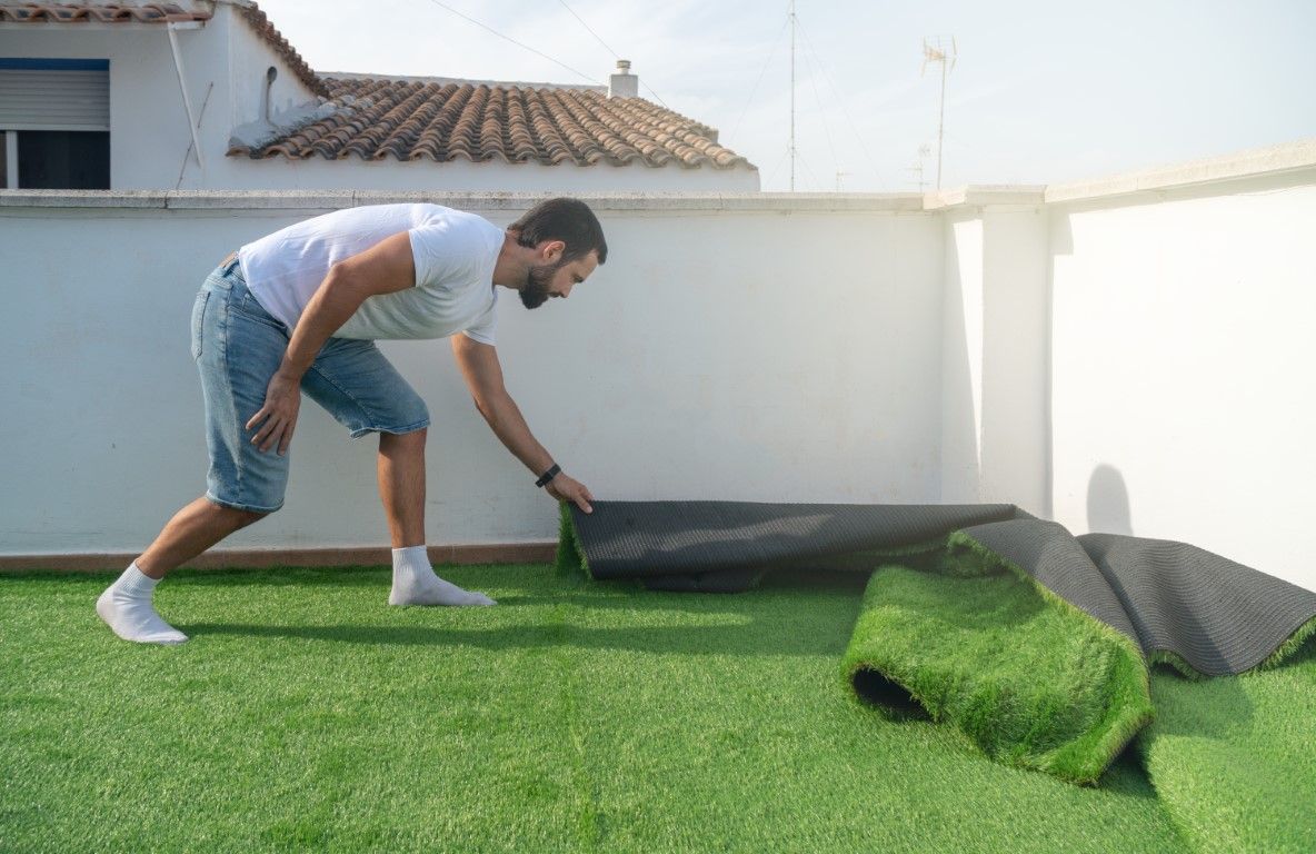 A person installing rolls of artificial grass on a white-walled rooftop patio.