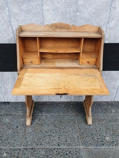 Escritorio de secretaría de madera con tallas florales ornamentadas sobre una superficie de baldosas grises.