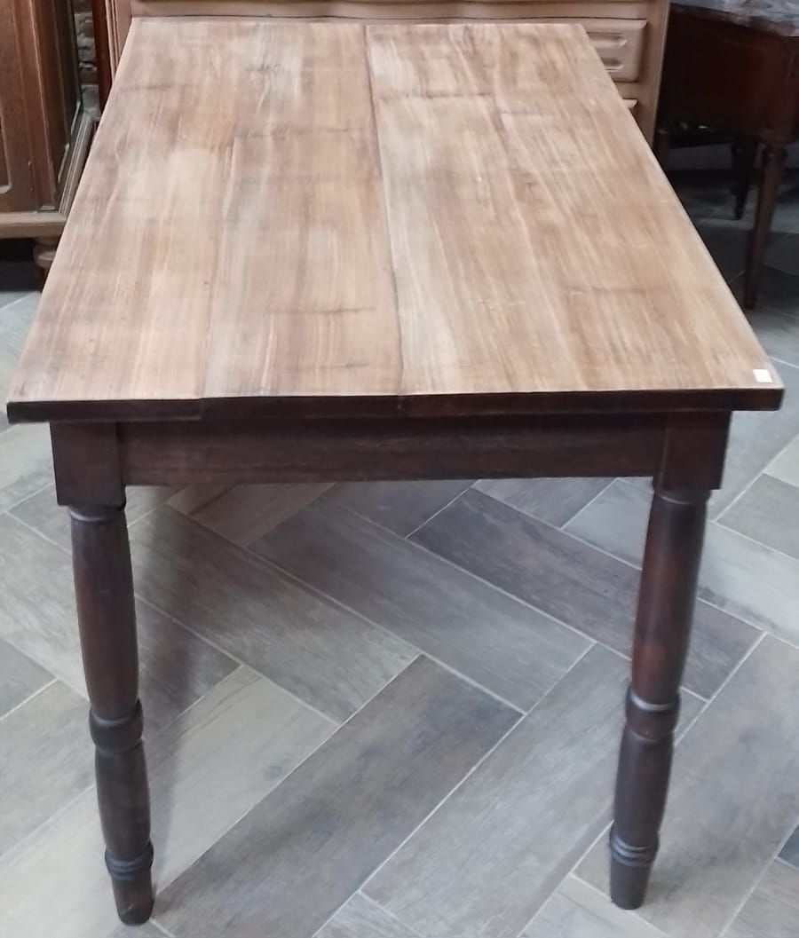 Mesa de comedor rectangular de madera con patas oscuras sobre suelo de baldosas en espiga.