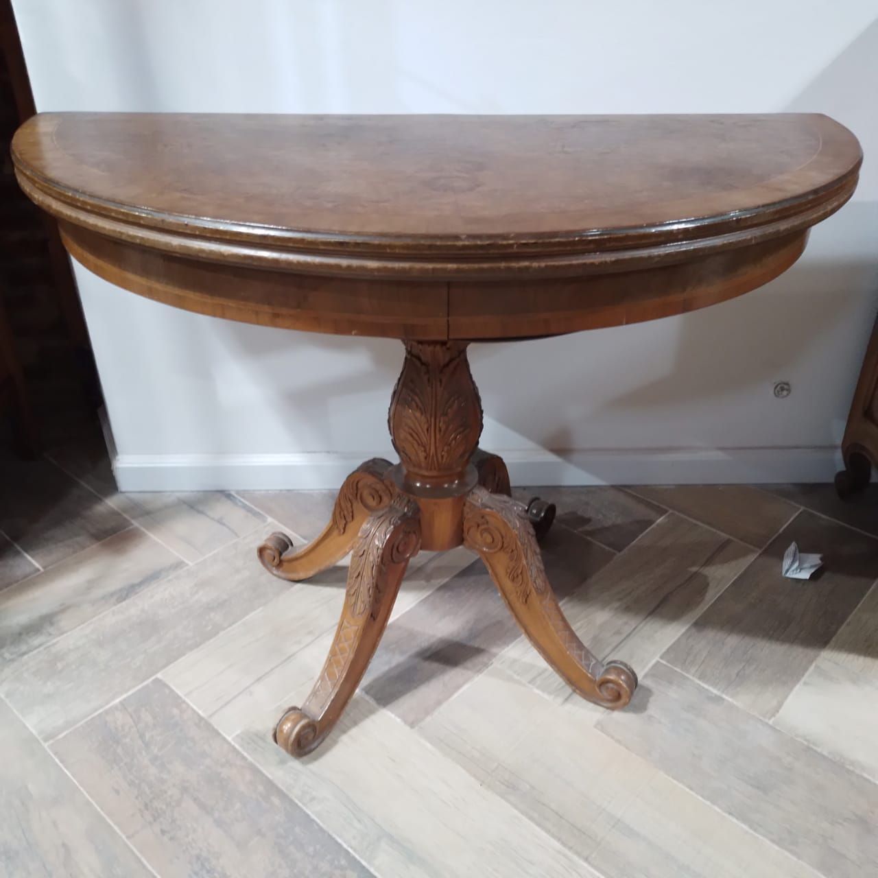 Mesa redonda con pedestal de madera. La mesa tiene un tablero de madera oscura con una costura y una base de pedestal tallada con tres patas.