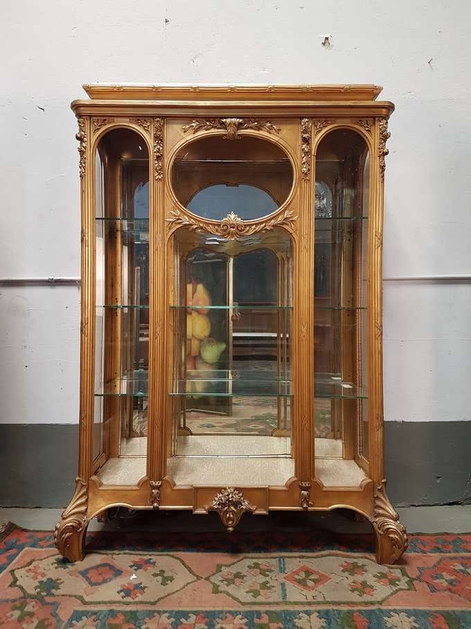 Vitrina de madera con estantes de cristal, tallas ornamentadas y parte posterior con espejo.