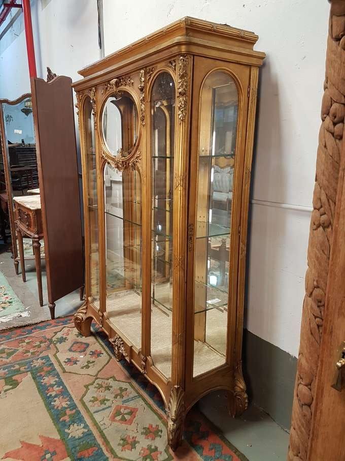 Vitrina de madera ornamentada con estantes de vidrio, tallas elaboradas y parte posterior con espejo.