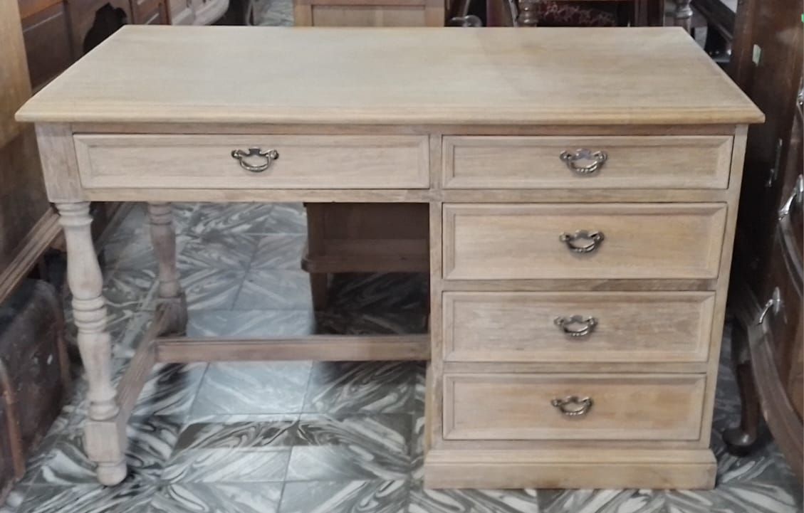 Escritorio de madera de color claro con varios cajones y una pata decorativa, sobre un fondo negro.