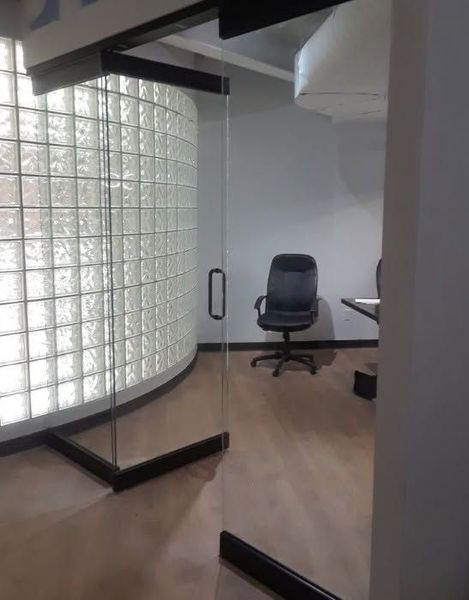 Office interior with glass door and curved glass block wall; chair and table visible inside.