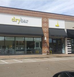 Exterior view of a Drybar salon with a black awning and yellow lettering on the sign.