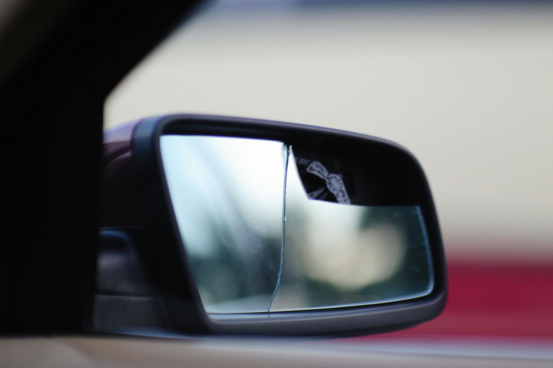 Broken side view mirror on a car. The glass is cracked, reflecting a blurred background.