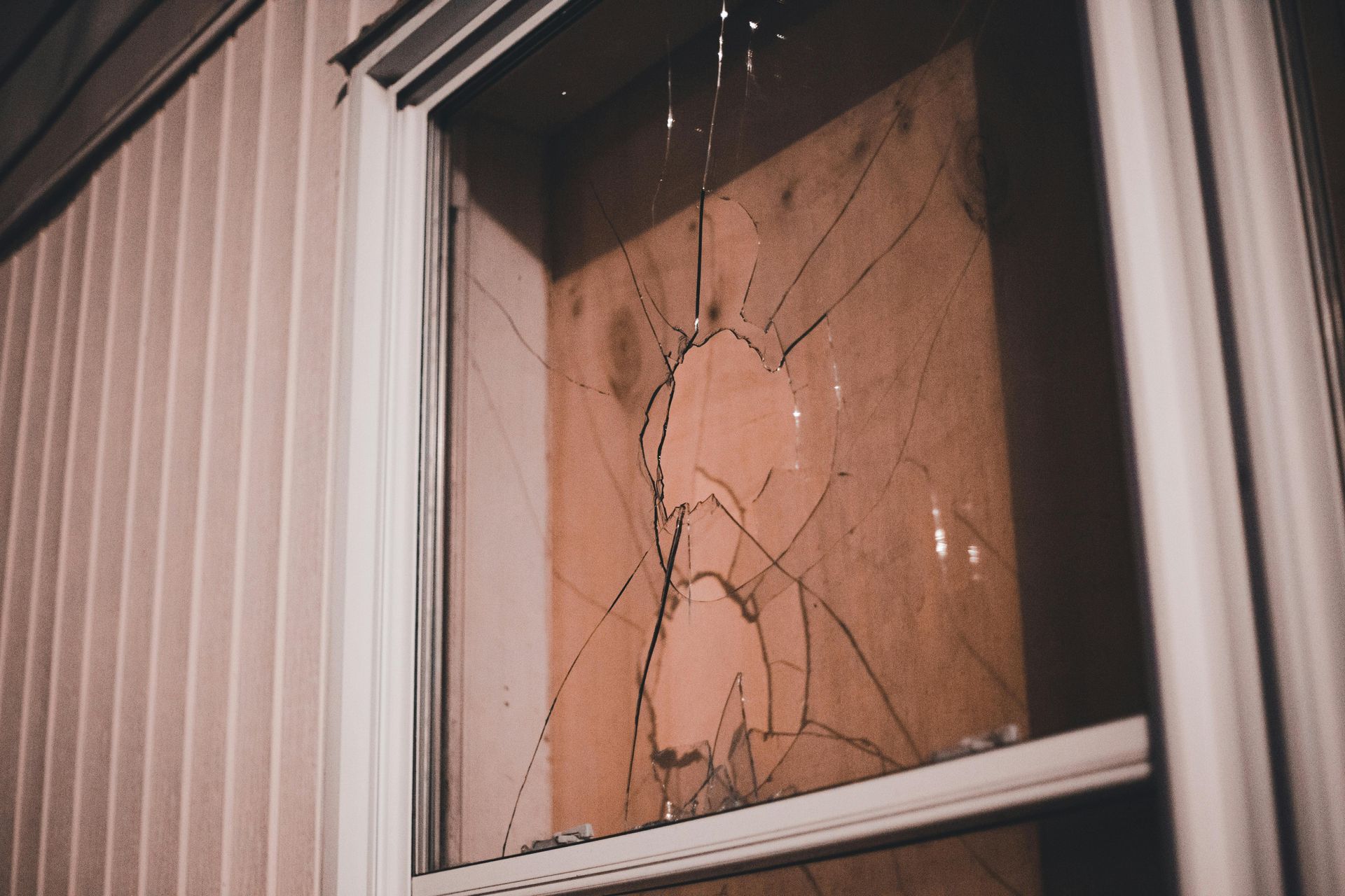 Shattered window, showing cracks radiating from a central point. Beige siding and window frame.