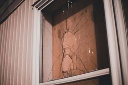 Shattered window, showing cracks radiating from a central point. Beige siding and window frame.