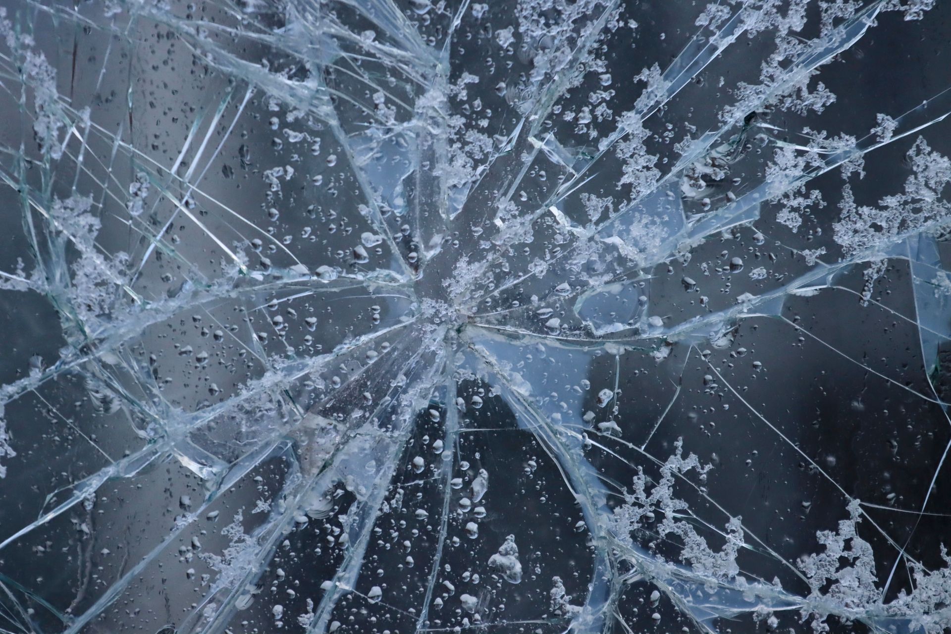 Cracked frosted glass with white spiderweb fractures against a dark background