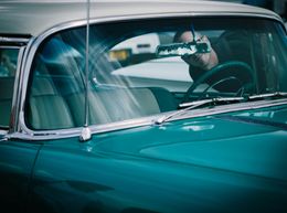 Teal and white classic car, partial view. Person at the steering wheel, clear windshield.