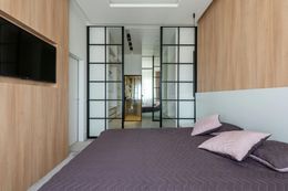 Bedroom with a large bed, wall-mounted TV, and glass-paneled sliding doors leading to another room.