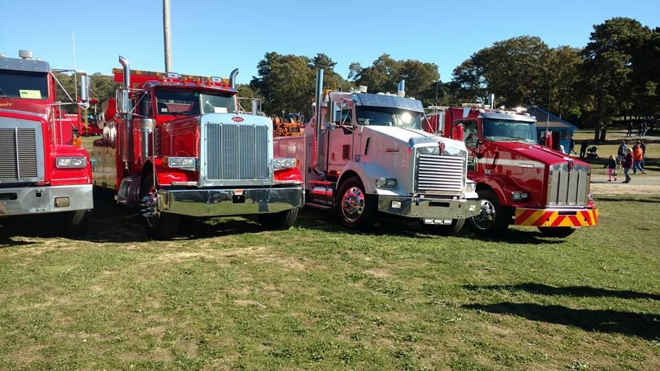 Several large red and silver semi-trucks parked on a grassy field on a sunny day.