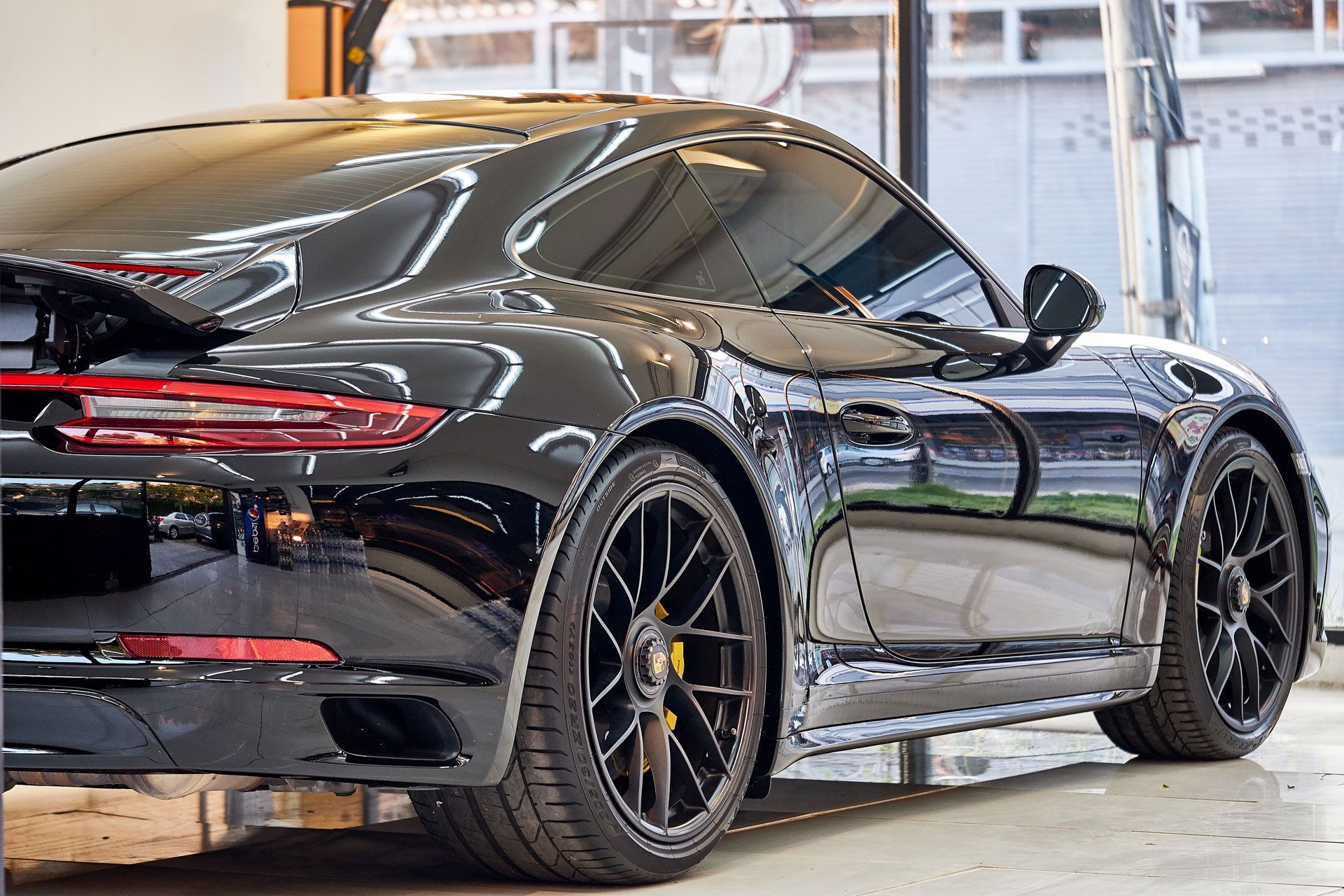 Black Porsche sports car parked indoors, reflecting surrounding light.