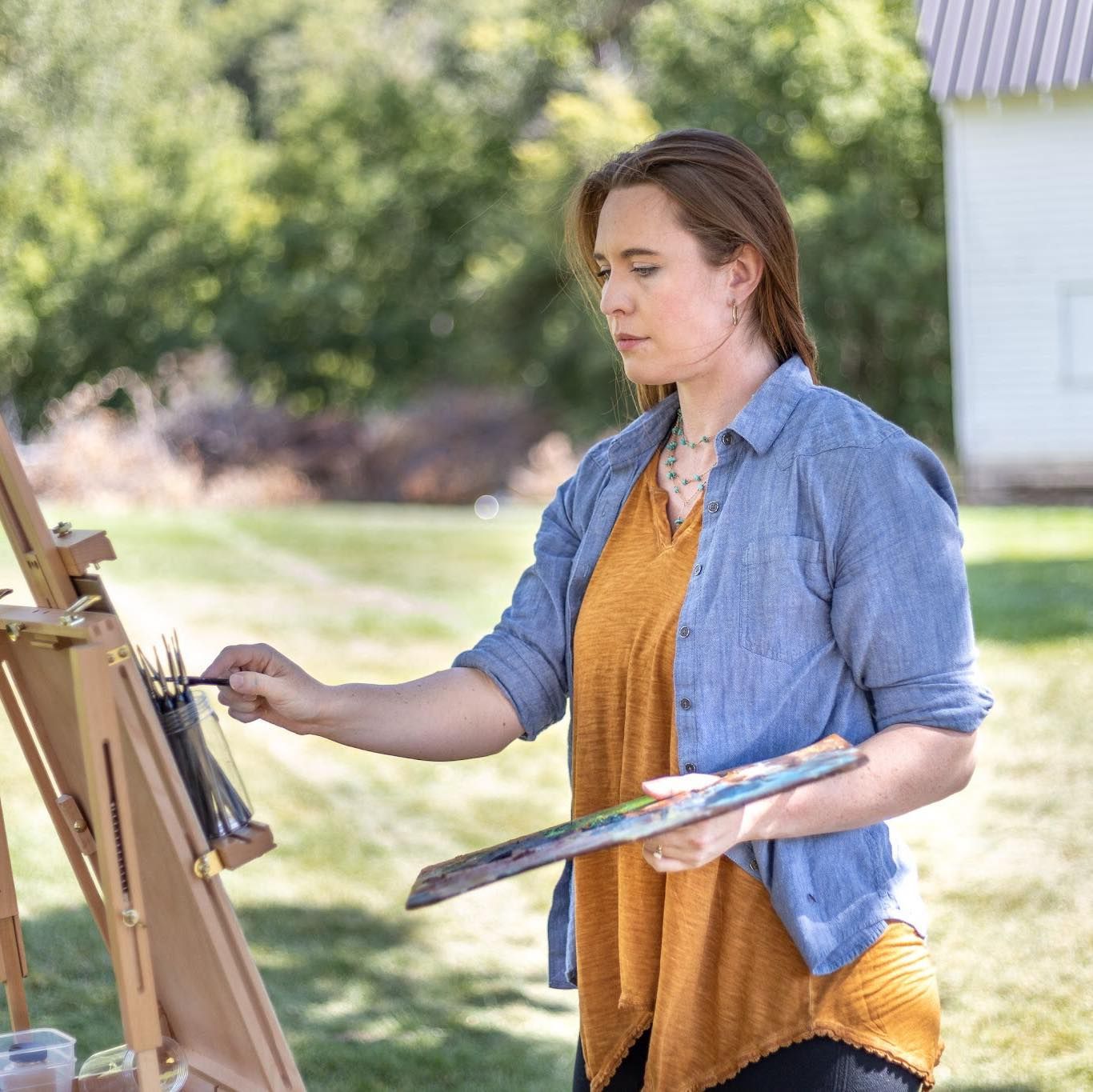 A woman is painting a picture on an easel outside.